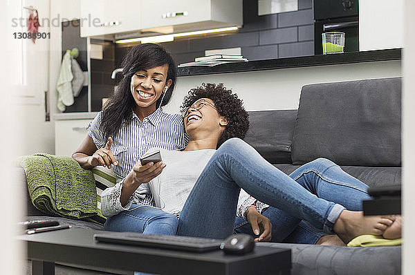 Glückliche Freunde unterhalten sich  während sie zu Hause Musik über ein Smartphone genießen