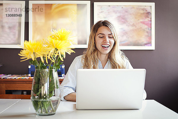 Fröhliche Frau mit Laptop und Vase auf dem Tisch zu Hause