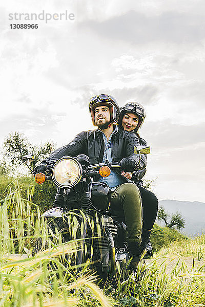 Ehepaar schaut weg  während es auf einem Motorrad gegen den Himmel sitzt