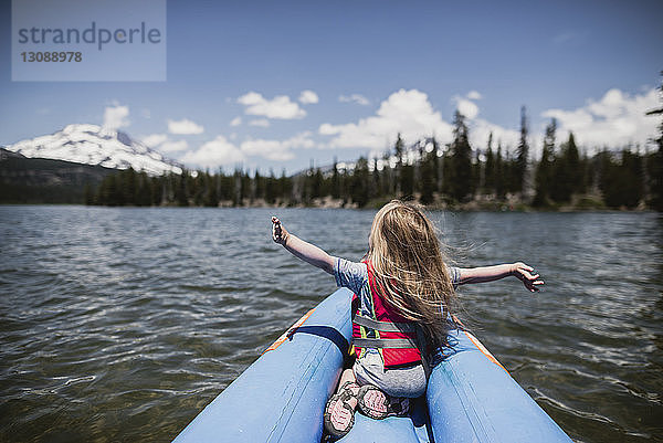 Rückansicht eines sorglosen Mädchens mit ausgestreckten Armen  das in einem aufblasbaren Floß auf dem See sitzt