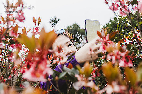 Wanderin fotografiert Pflanzen mit dem Handy  während sie gegen den Himmel steht