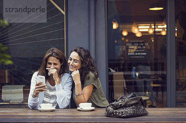 Glückliche reife Frauen mit Smartphone im Straßencafé