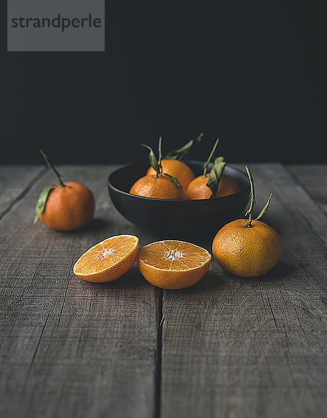 Orangen in Schale auf Holztisch vor schwarzem Hintergrund