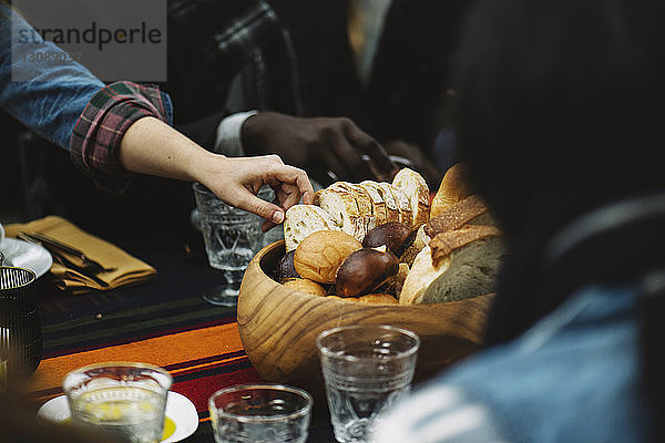 Frau nimmt Brot aus Holzschüssel  während sie mit einem Freund am Tisch sitzt