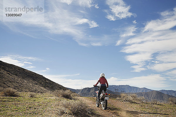 Rückansicht einer Motorrad fahrenden Frau auf Berg gegen Himmel