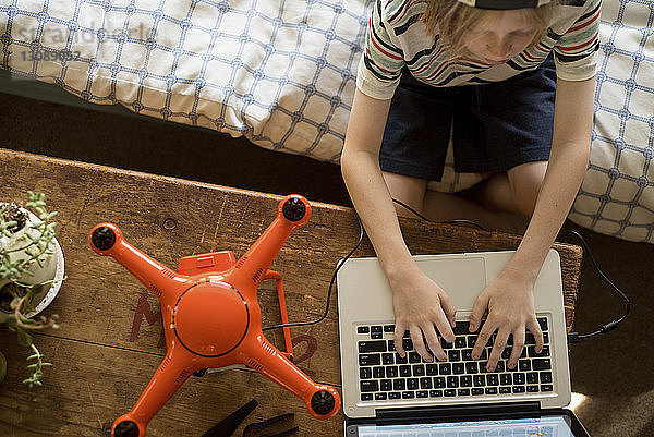 Draufsicht eines Jungen  der zu Hause mit einer Drohne an einem Laptop-Computer arbeitet