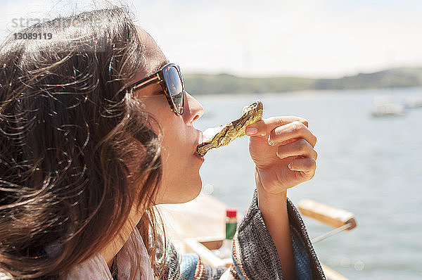 Nahaufnahme einer Frau  die an einem sonnigen Tag Austern gegen das Meer isst