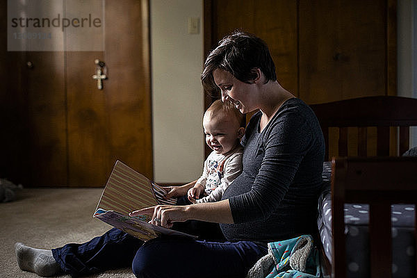 Schwangere Frau zeigt der Tochter ein Bilderbuch  während sie zu Hause sitzt