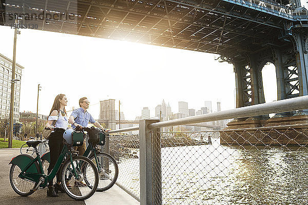 Paar mit Fahrrädern steht an der Promenade am East River vor der Manhattan-Brücke