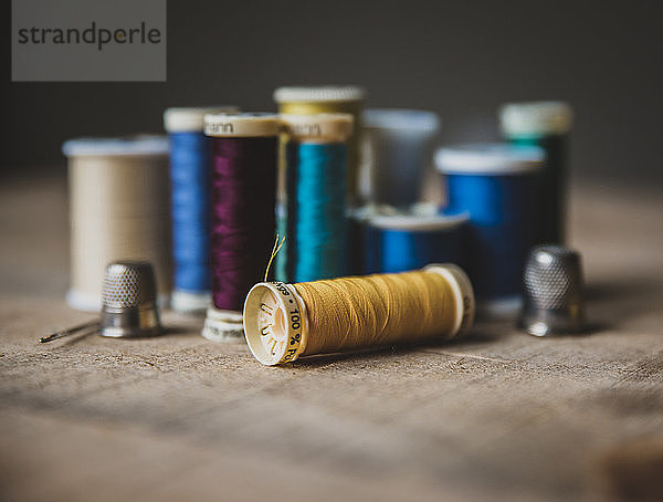 Nahaufnahme von bunten Spulen mit Fingerhüten auf Holztisch im Workshop