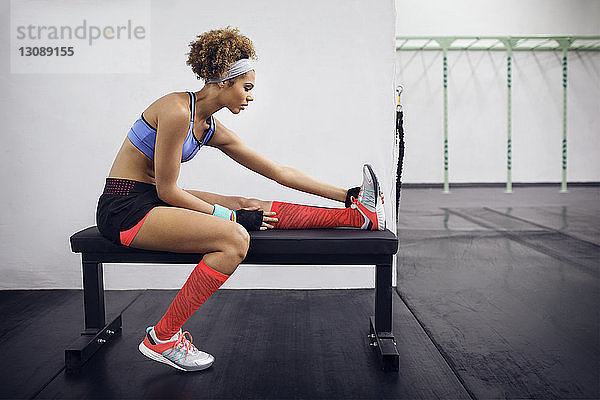 Seitenansicht einer Sportlerin  die auf einer Bank sitzend im Fitnessstudio trainiert
