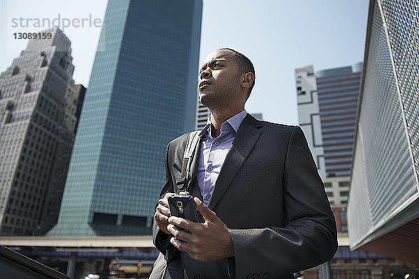 Niedriger Blickwinkel eines Geschäftsmannes  der sein Smartphone gegen Bürogebäude hält