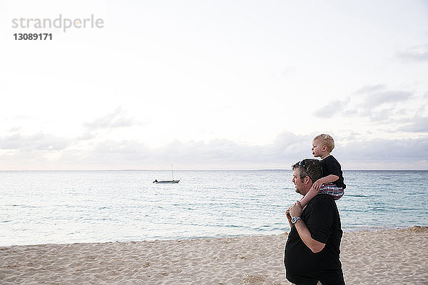 Glücklicher Vater trägt Sohn auf den Schultern  während er am Strand steht