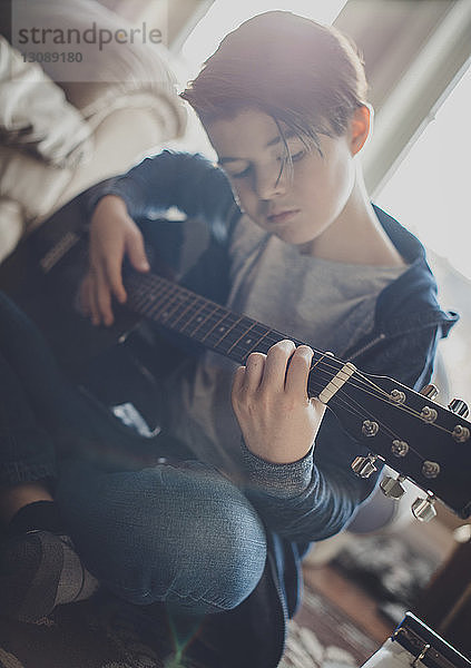 Junge spielt Gitarre  während er zu Hause sitzt