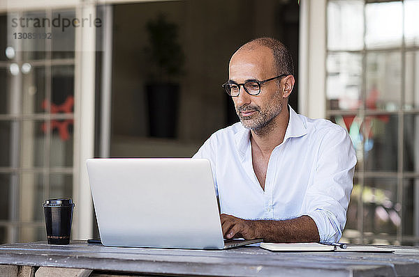 Geschäftsmann benutzt Laptop  während er im Büro am Tisch sitzt