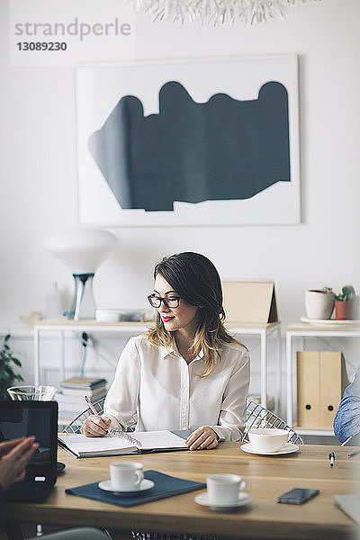 Lächelnde Geschäftsfrau schreibt  während sie im Büro am Schreibtisch sitzt