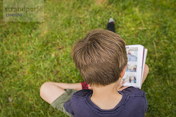 Hochwinkelansicht eines Jungen  der Comics liest  während er auf einem Grasfeld im Park sitzt