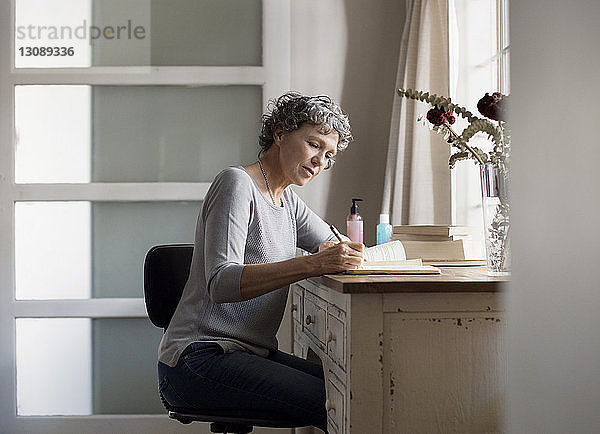 Reife Frau schreibt zu Hause in Buch auf den Tisch