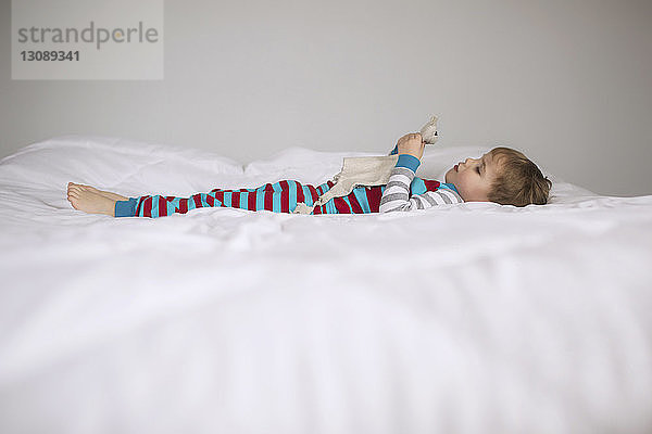 Seitenansicht eines Jungen  der Spielzeug hält  während er zu Hause auf dem Bett liegt