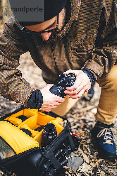 Hochwinkelansicht der Kamera eines Wanderers  der die Kamera einstellt  während er auf einem Feld im Wald kniet