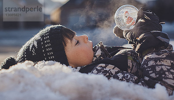 Seitenansicht eines Jungen mit Schneekugel  der im Winter im Freien liegt