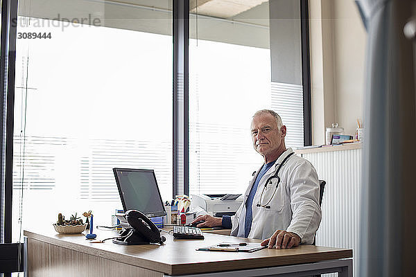 Porträt eines Arztes  der im Krankenhaus am Schreibtisch am Fenster arbeitet
