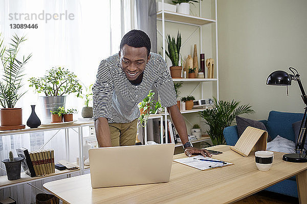 Glücklicher Mann mit Laptop am Tisch im Heimbüro