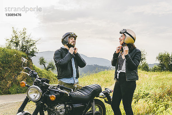 Paar trägt Helme  während es mit dem Motorrad gegen den Himmel steht