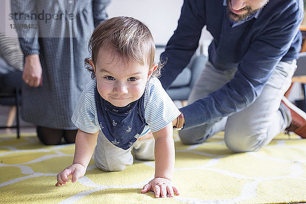 Glückliche Eltern sehen ihren Sohn zu Hause auf dem Teppich krabbeln