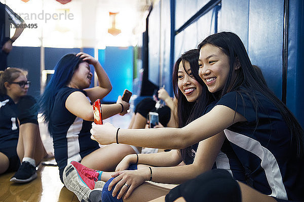 Fröhliche Mädchen  die mit ihrem Smartphone auf dem Volleyballfeld sitzen