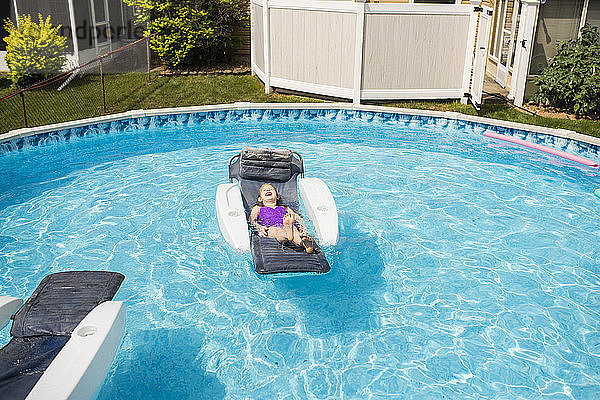 Glückliches Mädchen entspannt sich auf einem aufblasbaren Floß im Schwimmbad