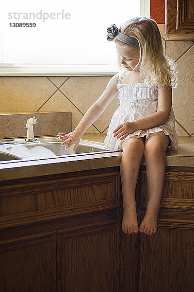 Mädchen spielt mit Seifenlauge in der Spüle  während sie zu Hause auf dem Küchentisch sitzt