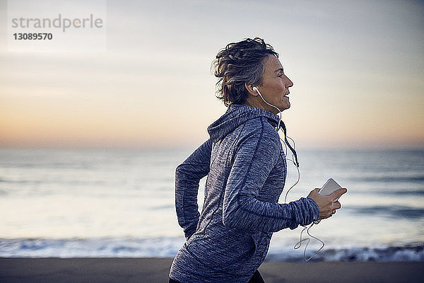 Frau joggt beim Musikhören am Strand gegen den Himmel