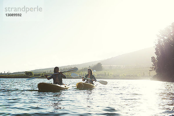 Fröhliche Freundinnen beim Kajakfahren auf dem See bei klarem Himmel an einem sonnigen Tag