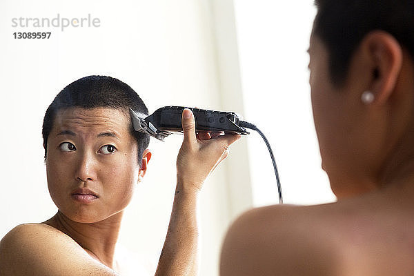 Frau rasiert sich die Haare  während sie im Spiegel reflektiert