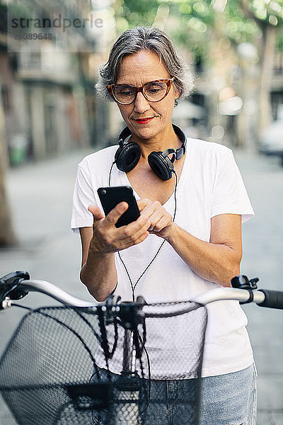 Frau benutzt Smartphone  während sie mit dem Fahrrad auf der Straße steht