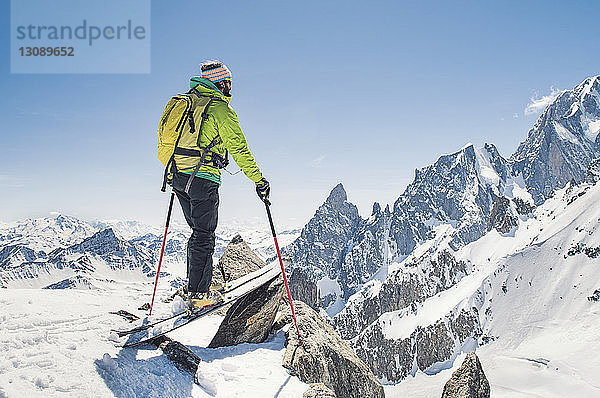 Wanderer mit Skiern auf schneebedecktem Berg bei strahlend blauem Himmel am sonnigen Tag