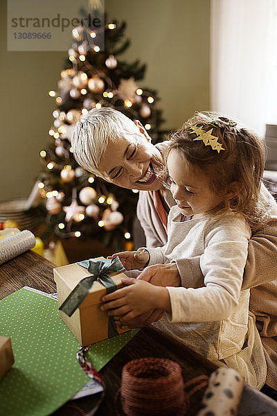Glückliche Großmutter schaut auf ein Mädchen  das am Tisch ein Geschenk verpackt