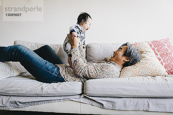 Glücklicher Großvater spielt mit seinem Enkel  während er zu Hause auf dem Sofa liegt