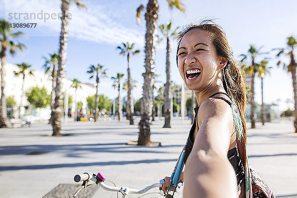 Porträt einer fröhlichen Frau  die im Sommer auf der Strasse Fahrrad fährt