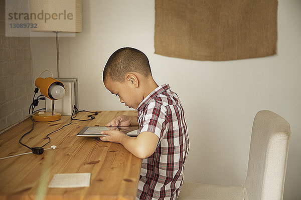 Seitenansicht eines Jungen mit Tablet-Computer am Tisch an der Wand