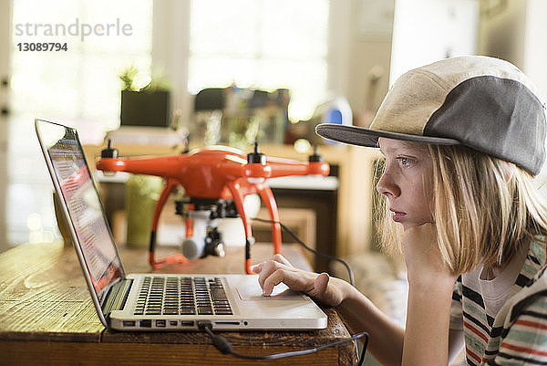 Seitenansicht eines Jungen  der zu Hause mit einer Drohne am Laptop arbeitet