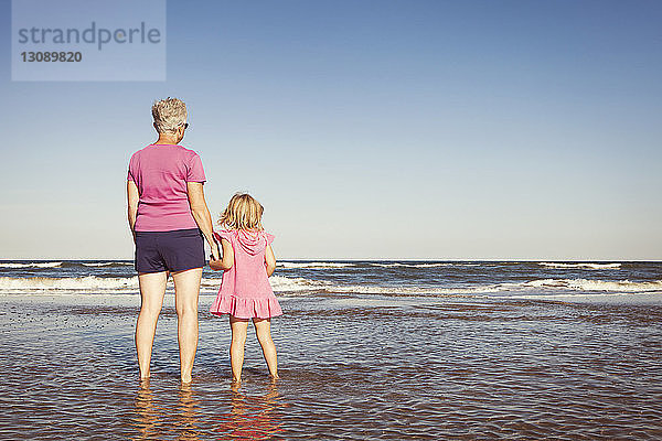 Enkelin und Großmutter stehen im Meer vor klarem Himmel