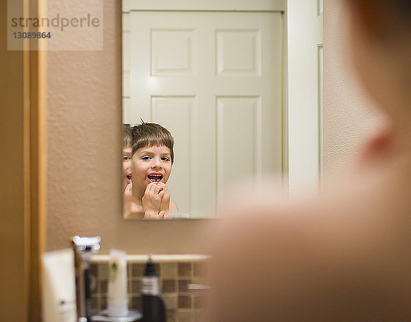 Porträt eines Jungen  der zu Hause eine Zahnlücke zeigt  die sich im Spiegel spiegelt