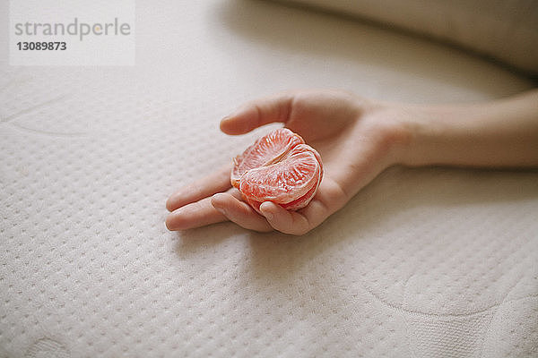 Geschorene Hand einer Frau  die zu Hause eine Pampelmuse auf dem Bett hält