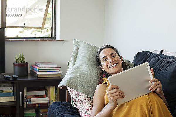 Porträt einer schwangeren Frau  die einen Tablet-Computer benutzt  während sie zu Hause auf dem Sofa liegt