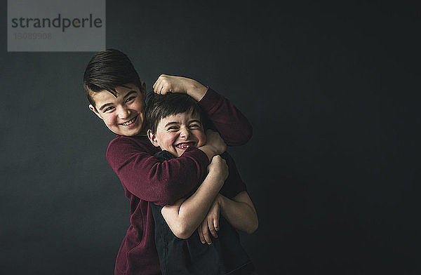 Porträt eines glücklichen Jungen  der mit seinem Bruder spielt  während er an der Wand steht