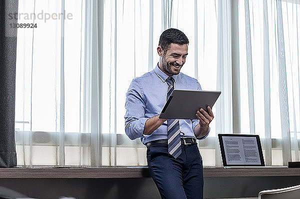 Glücklicher Geschäftsmann mit Tablet-Computer am Fenster im Hotelzimmer