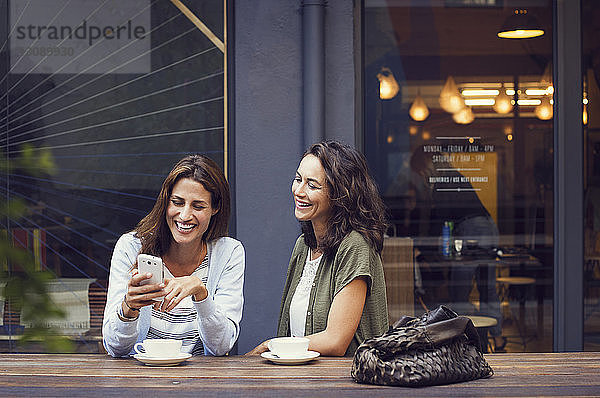 Glückliche Freundinnen mit Smartphone im Straßencafé