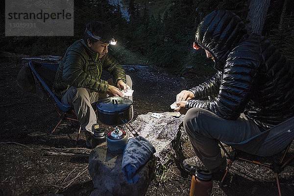 Freunde spielen Kartenspiel beim Camping im Wald in der Dämmerung